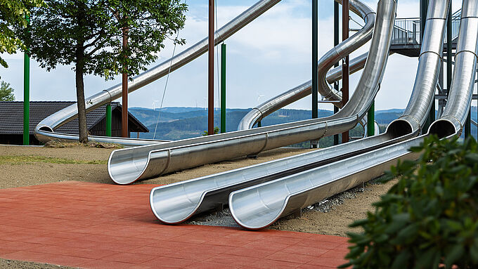 Mehrere Edelstahlrutschen enden auf einer roten Fläche aus REGUPOL playfix FX50 Fallschutzplatten im Panorama Park Sauerland